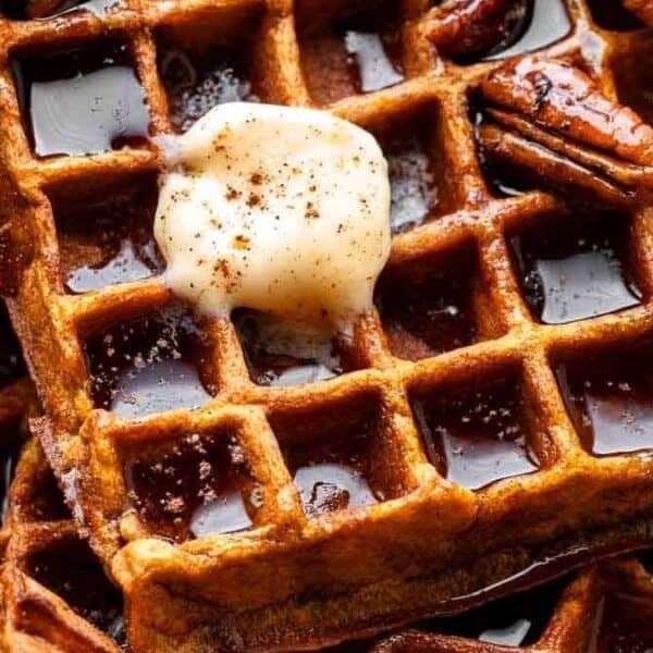 Waffles with a pat of butter, pecans, and syrup on top.
