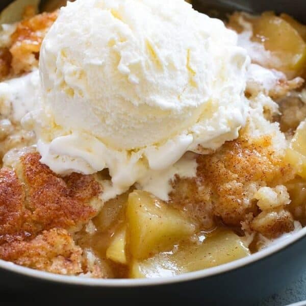 A bowl containing apple cobbler with a scoop of vanilla ice cream on top.