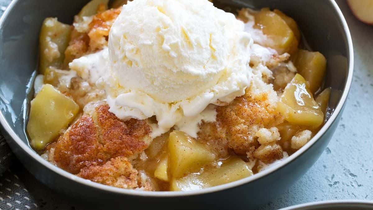 A bowl containing apple cobbler with a scoop of vanilla ice cream on top.