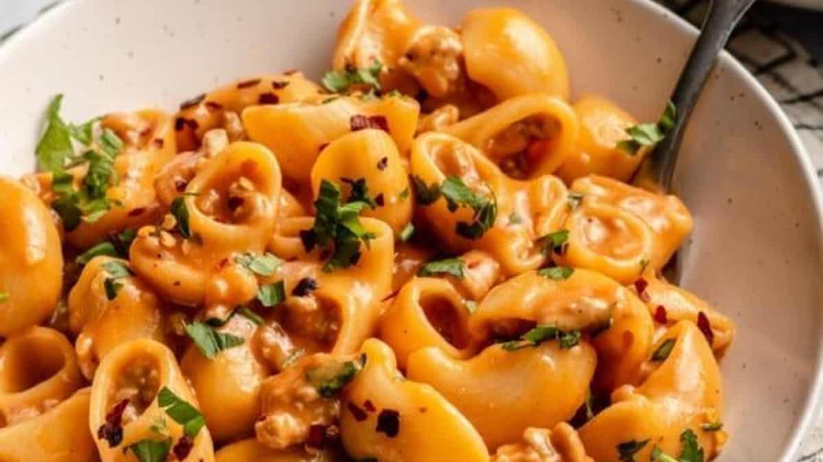 Pasta shells in creamy tomato sauce, topped with chopped parsley and red pepper flakes, served in a bowl with a fork beside.