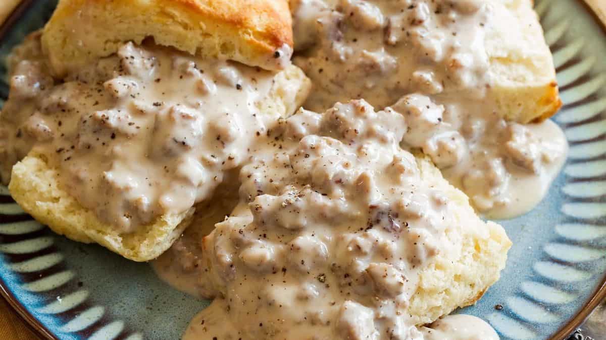Biscuits topped with creamy sausage gravy are served on a blue patterned plate.