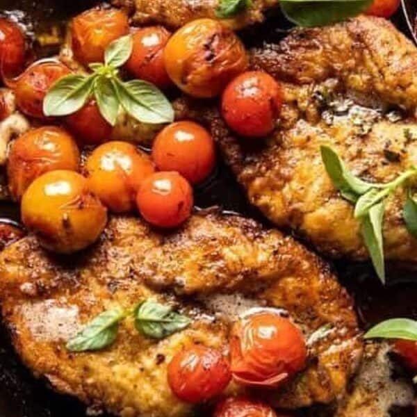 Pan-seared chicken breasts, roasted cherry tomatoes, fresh basil, and light sauce in a black skillet.