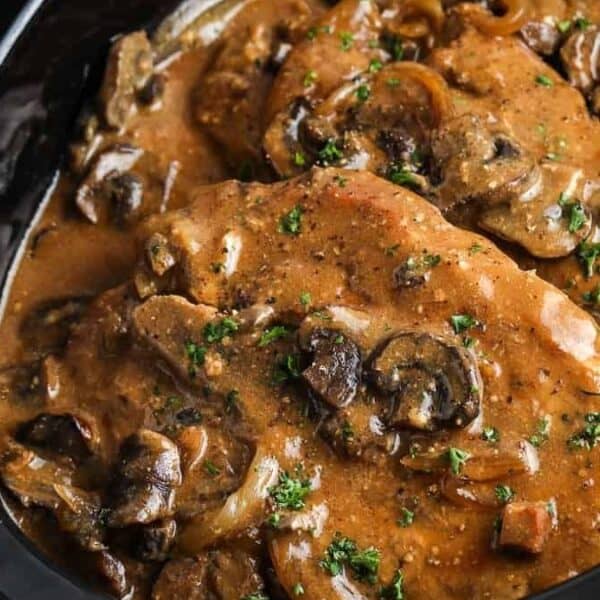 Sliced beef topped with creamy brown mushroom sauce and chopped herbs in a black slow cooker.