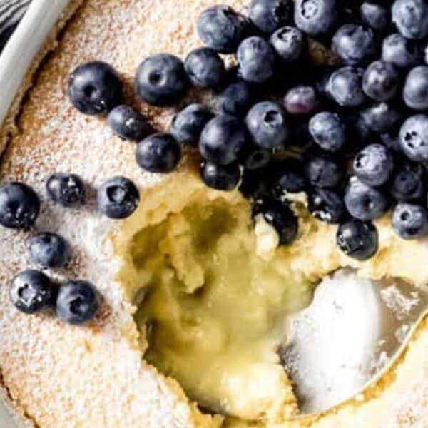 Baked dessert with fresh blueberries and powdered sugar on top; a spoon is scooping from the center.