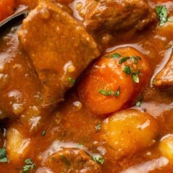Chunks of beef, carrots, and potatoes in thick brown broth, topped with chopped herbs in a bowl.