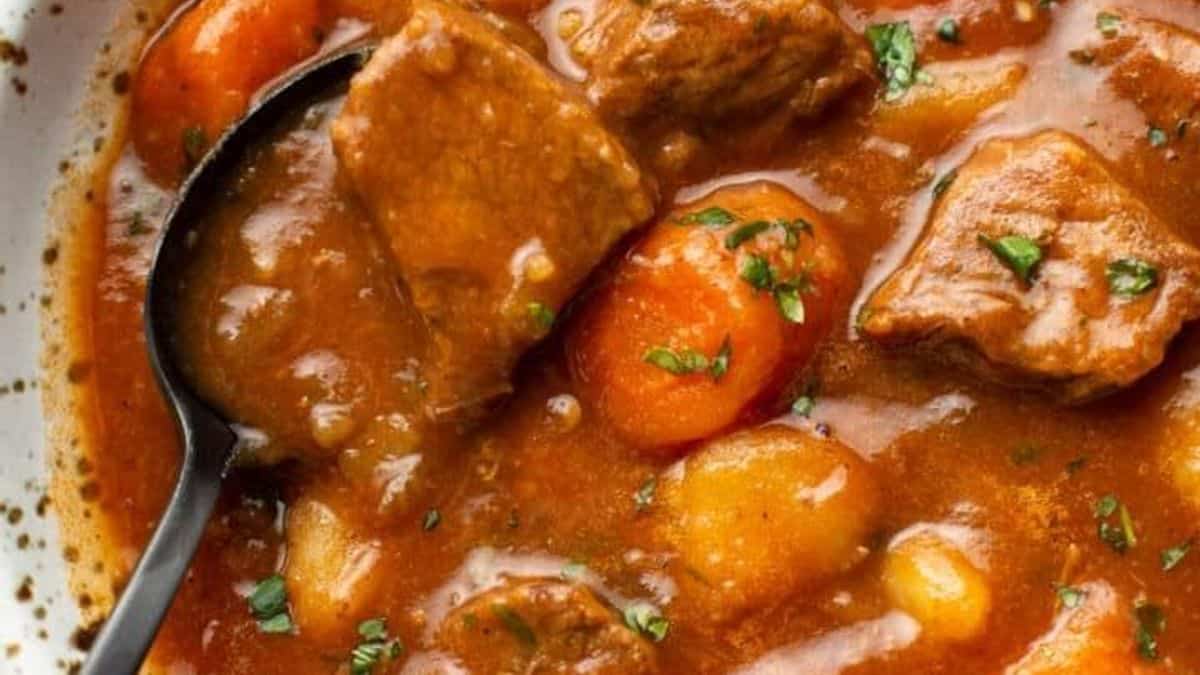 Chunks of beef, carrots, and potatoes in thick brown broth, topped with chopped herbs in a bowl.