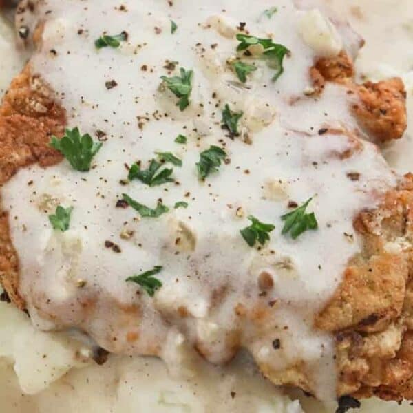 Chicken fried steak with white gravy and parsley on mashed potatoes, served on a white plate with a fork.