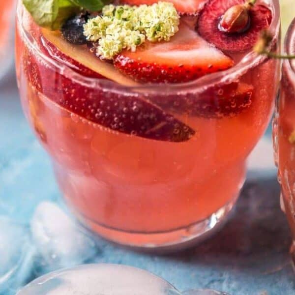 Three glasses of pink fruit punch with sliced strawberries, cherries, and edible flowers on a blue surface with ice.
