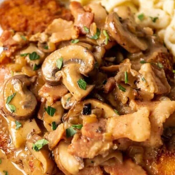 Breaded meat with creamy mushroom and bacon sauce next to a serving of small pasta noodles on a plate.