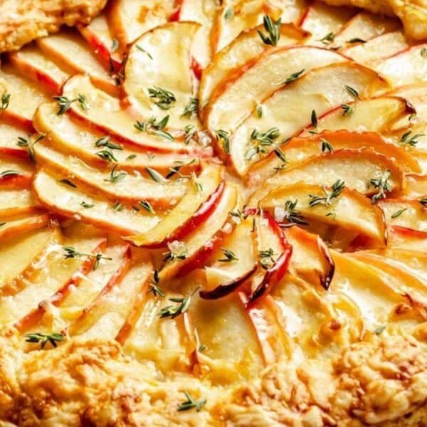 A rustic apple galette with thinly sliced apples layered on a flaky crust, topped with fresh green herbs.