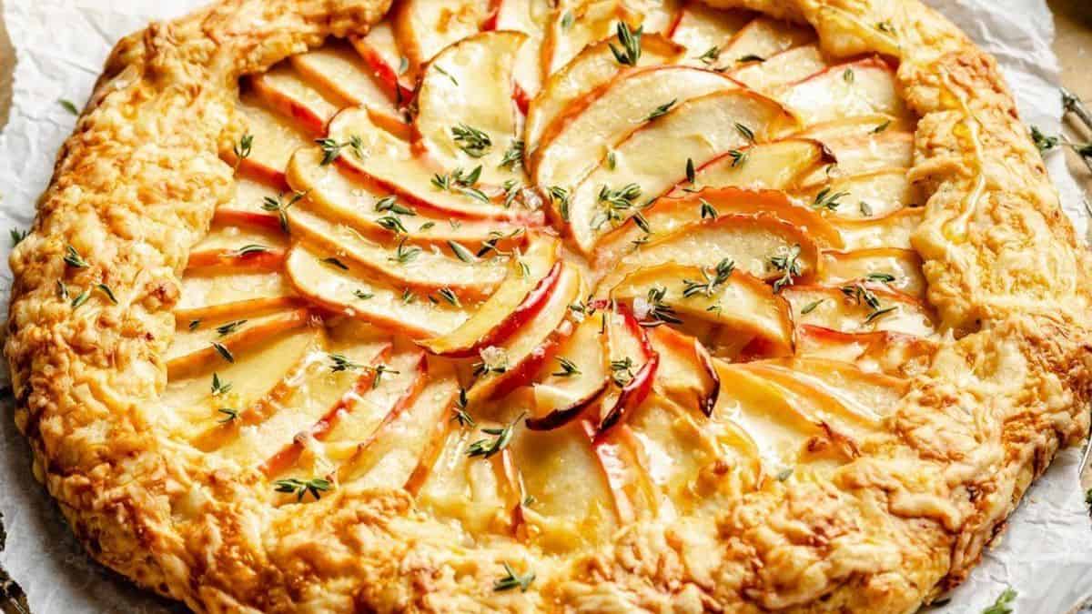 A rustic apple galette with thinly sliced apples layered on a flaky crust, topped with fresh green herbs.