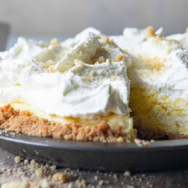 A pie with a crumbly crust, creamy yellow filling, and whipped topping in a metal dish with one slice missing.