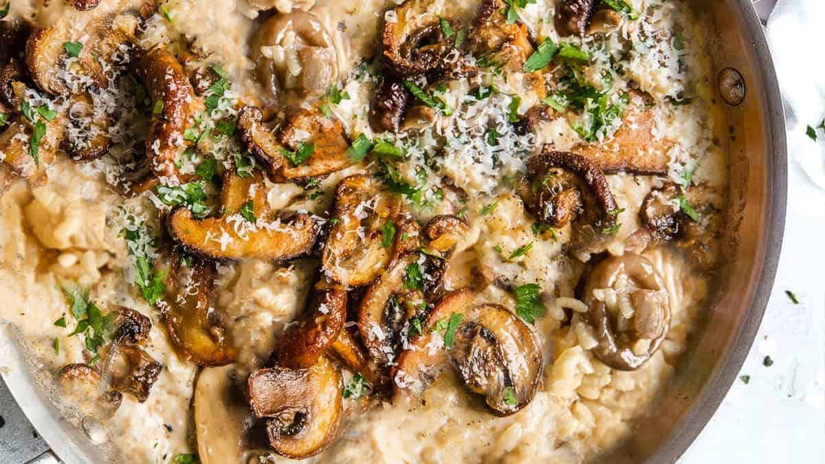 Creamy risotto with mushrooms, chopped parsley, and grated cheese in a metal pan.