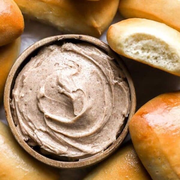 A bowl of cinnamon butter surrounded by several golden brown dinner rolls.