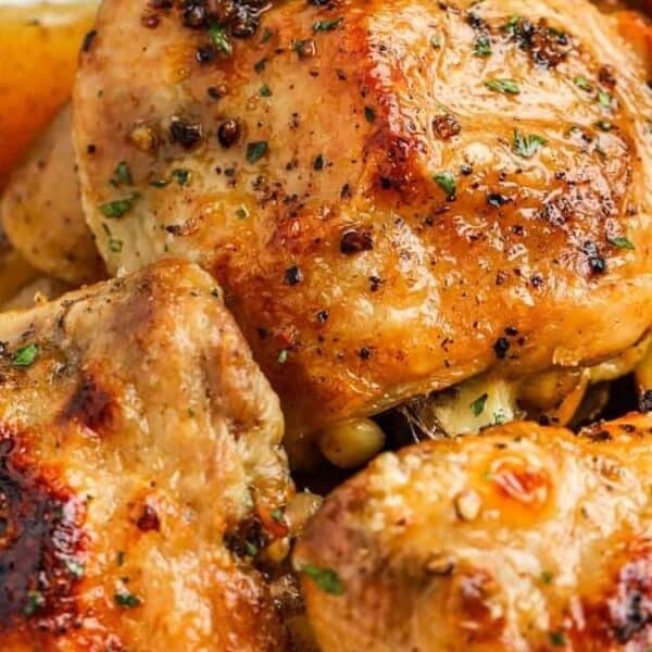 Roasted chicken thighs, potatoes, and carrots with herbs on a white plate.