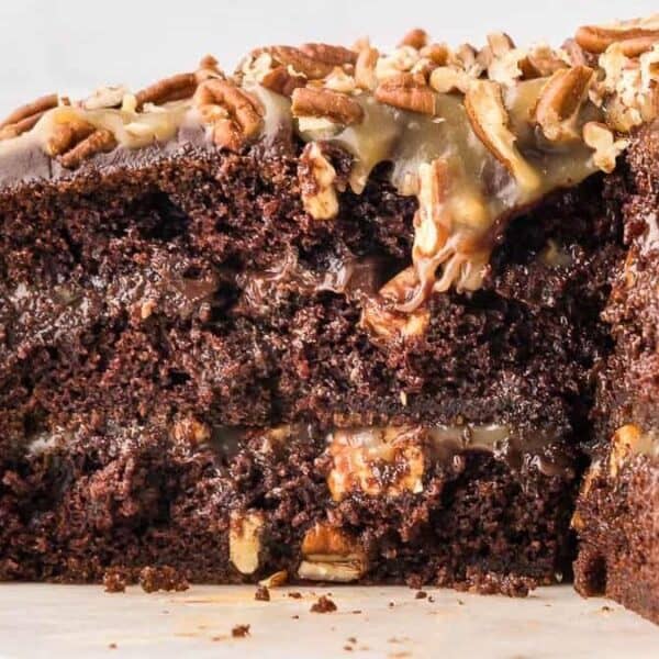 Sliced chocolate cake with caramel and chocolate layers, topped with chopped pecans.