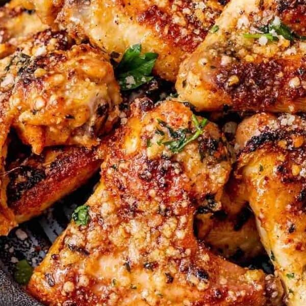 Crispy baked chicken wings in a pan, topped with grated cheese, herbs, and sprinkled seasonings.