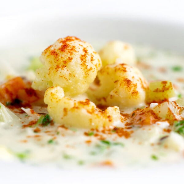 A bowl filled with creamy soup, topped with cauliflower florets, chopped herbs, and a dusting of paprika.