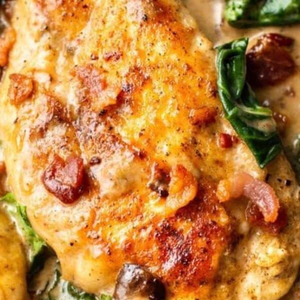 Chicken breasts, creamy sauce, mushrooms, spinach, and bacon pieces cooked together in a skillet.