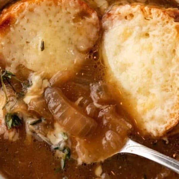 A bowl of French onion soup with toasted bread slices topped with melted cheese and a spoon resting inside.