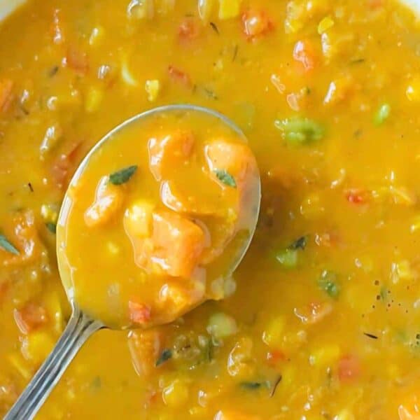 A bowl of thick, yellow vegetable soup containing carrots and greens, with a spoon lifting some soup from the bowl.