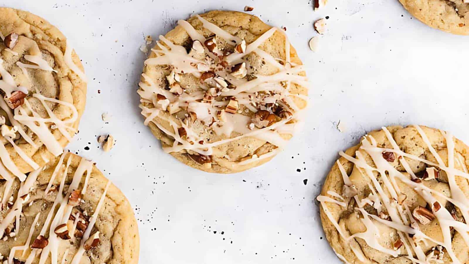 Five cookies topped with chopped nuts and drizzled icing are arranged on a white surface.