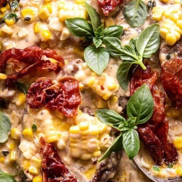 Creamy corn, crispy prosciutto, chicken, and fresh basil leaves in a skillet.