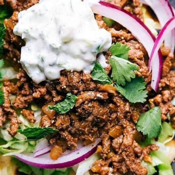 Seasoned ground beef, sliced red onions, lettuce, cilantro, and a dollop of creamy sauce on a taco salad.