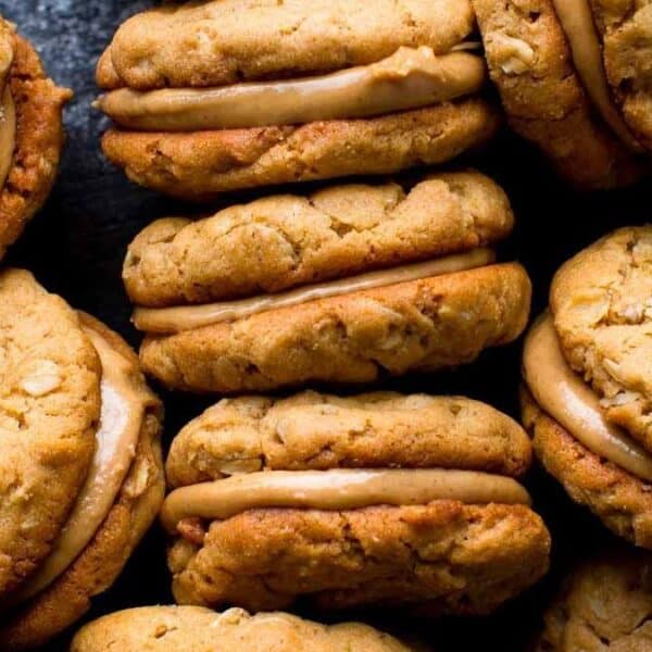 Several oatmeal sandwich cookies with creamy peanut butter filling on a dark surface.