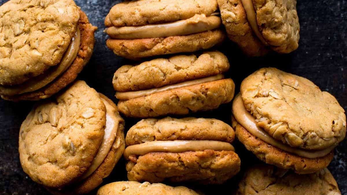 Several oatmeal sandwich cookies with creamy peanut butter filling on a dark surface.