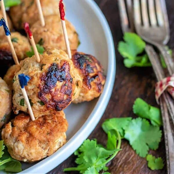 Browned meatballs with toothpicks and cilantro on a plate beside forks bundled together with a checked ribbon.