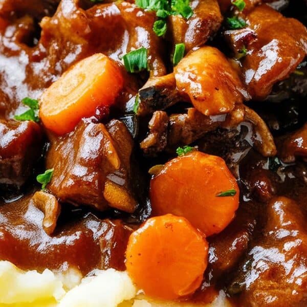 A close-up of beef stew with chunks of carrot and rich gravy served over creamy mashed potatoes.
