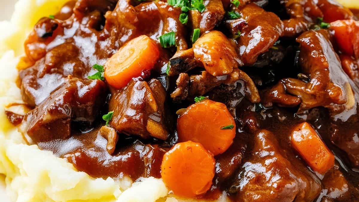 A close-up of beef stew with chunks of carrot and rich gravy served over creamy mashed potatoes.