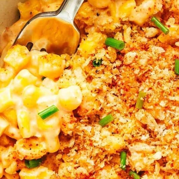Creamy baked corn casserole topped with breadcrumbs, chopped chives, and paprika, with a spoon scooping some out.