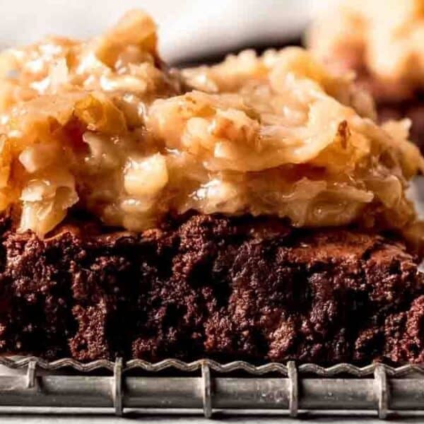 A brownie with a thick layer of coconut and pecan frosting on top rests on a metal wire cooling rack.