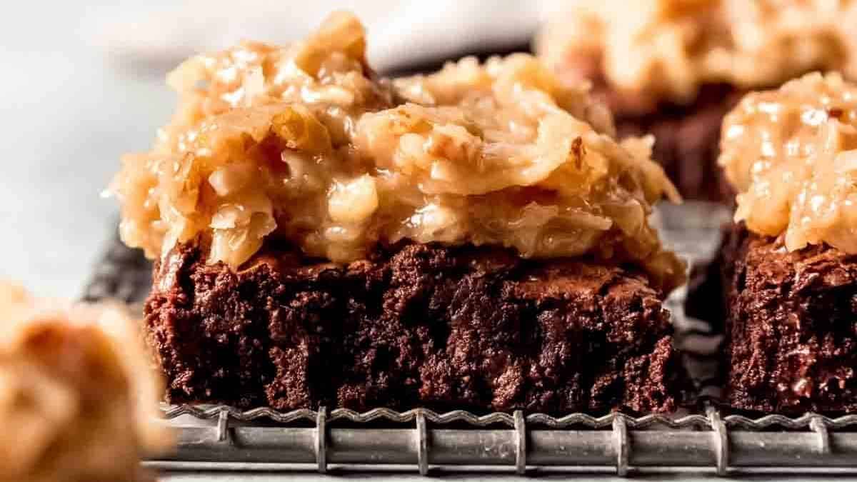 Chocolate brownie with coconut and caramel frosting on top, sitting on a cooling rack.