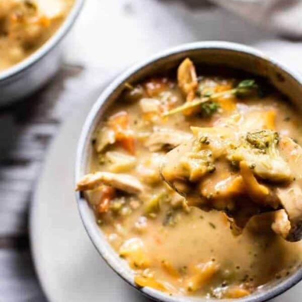 A close-up of a spoonful of thick chicken and vegetable soup being lifted from a mug, with another bowl in the background.