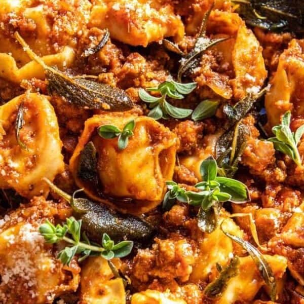 Tortellini pasta covered in meat sauce, topped with fresh herbs and grated cheese on a white plate.