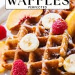 Plate of waffles topped with banana slices, peach slices, raspberries, and powdered sugar.