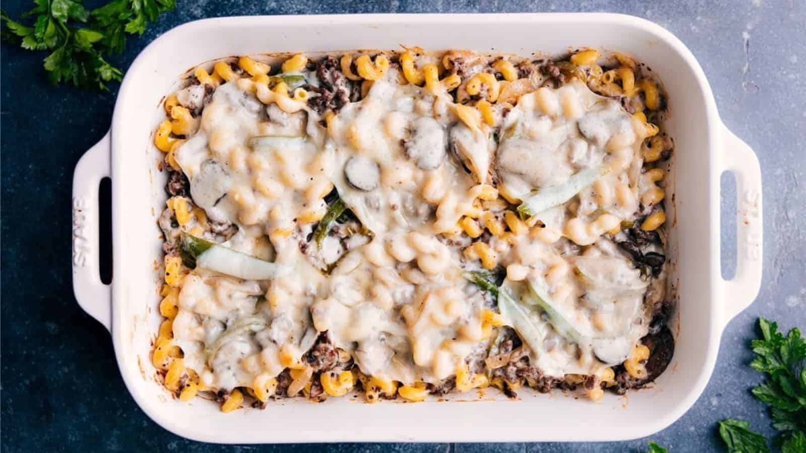 A white baking dish filled with baked pasta, melted cheese on top, ground meat, and pieces of green vegetables.