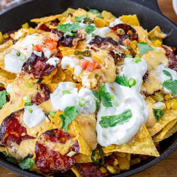 Nachos in a cast iron skillet, topped with melted cheese, jalapeños, diced tomatoes, sour cream, green onions, and cilantro.
