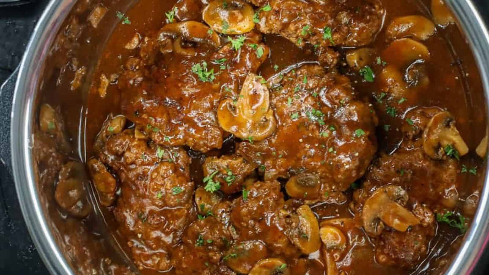A pot containing Salisbury steak patties in brown mushroom gravy, topped with chopped parsley.