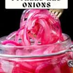 A fork lifts sliced pickled red onions from a glass jar with pink brine, text overlay reads “Sweet and Spicy Pickled Red Onions.”.