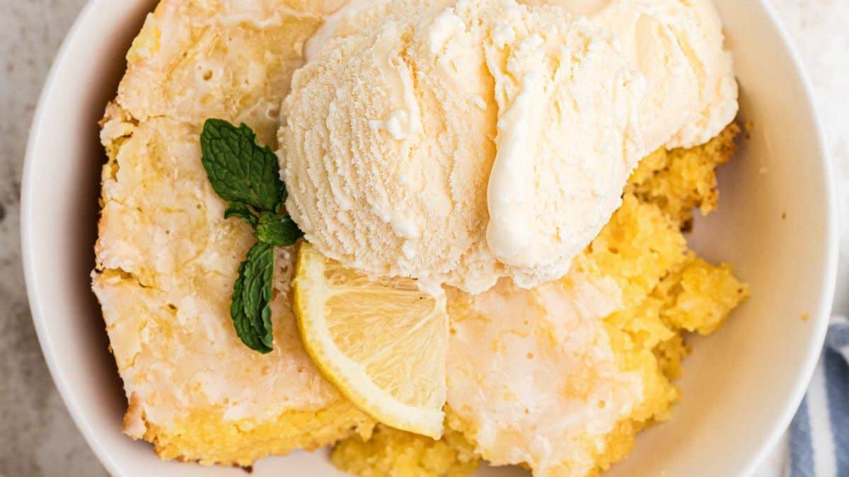 A bowl of lemon dessert topped with vanilla ice cream, garnished with a mint sprig and a lemon slice.