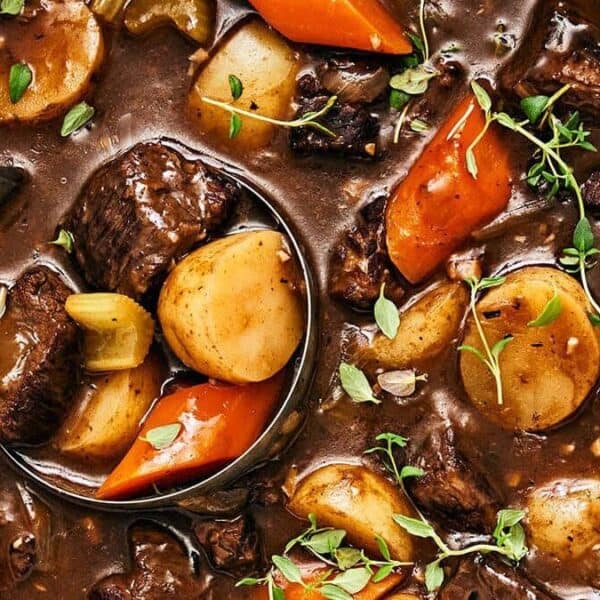 Chunks of beef, potatoes, carrots, and celery in thick brown broth with fresh herb garnish.