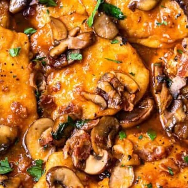 Chicken cutlets in brown sauce with mushrooms, bacon, and herbs, topped with chopped parsley.