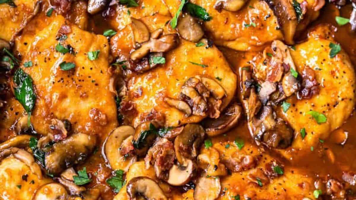 Chicken cutlets topped with brown sauce, sautéed mushrooms, crispy bacon pieces, and garnished with fresh herbs.