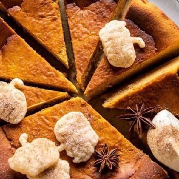 Sliced round pumpkin pie topped with whipped cream, small leaf-shaped cookies, and decorated with star anise.