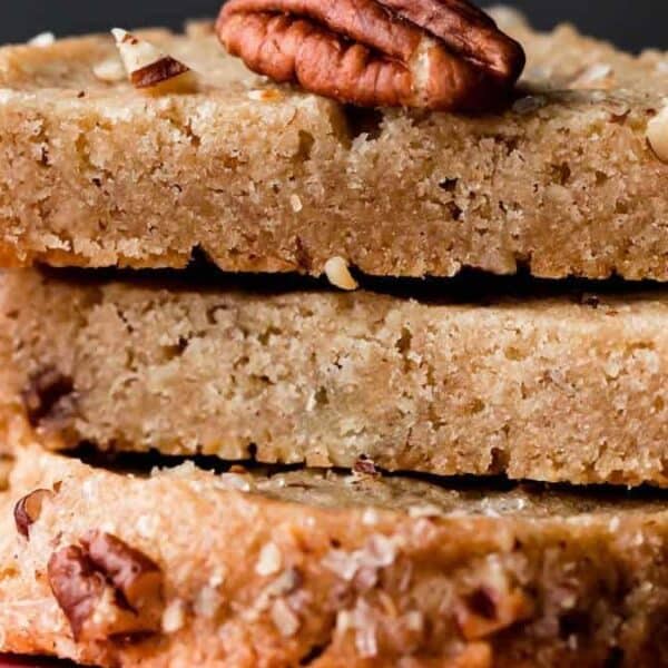 Three stacked pecan shortbread cookies, each topped with a whole pecan and sprinkled with sugar crystals.