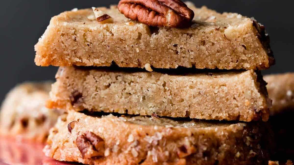 Three stacked pecan shortbread cookies, each topped with a whole pecan and sprinkled with sugar crystals.